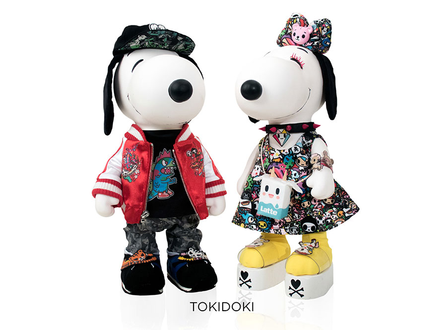 Two black and white, stuffed toy dogs in front of a white background. One is wearing a colourful dress and the other one a red jacket with colourful pants and a baseball hat.
