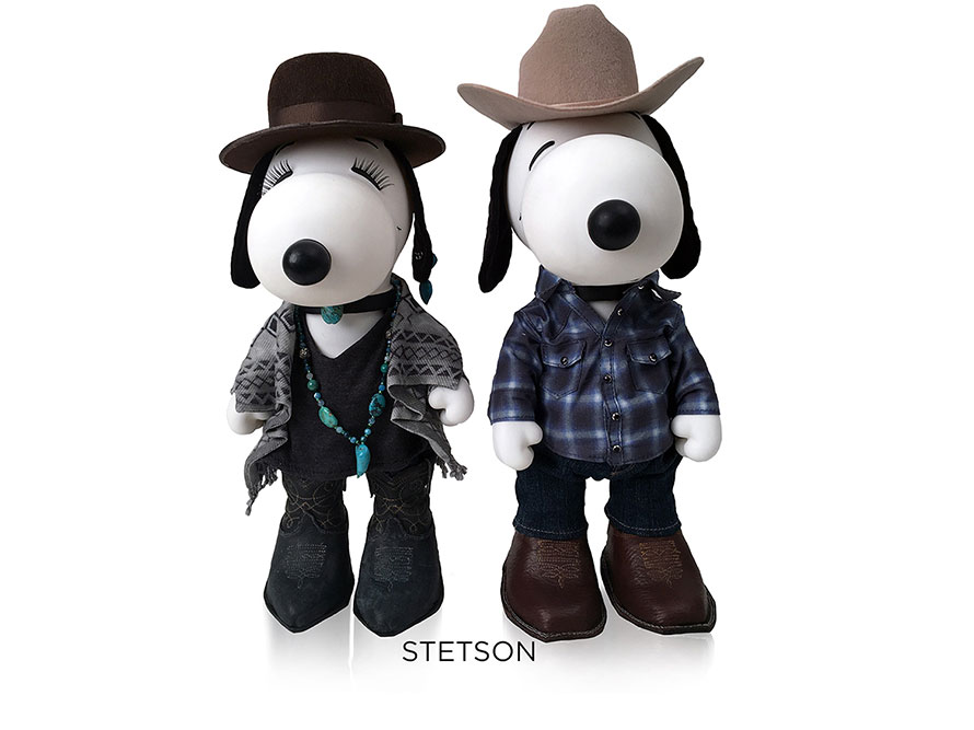 Two black and white, stuffed toy dogs standing in front of a white background wearing cowboy and cowgirl costumes.