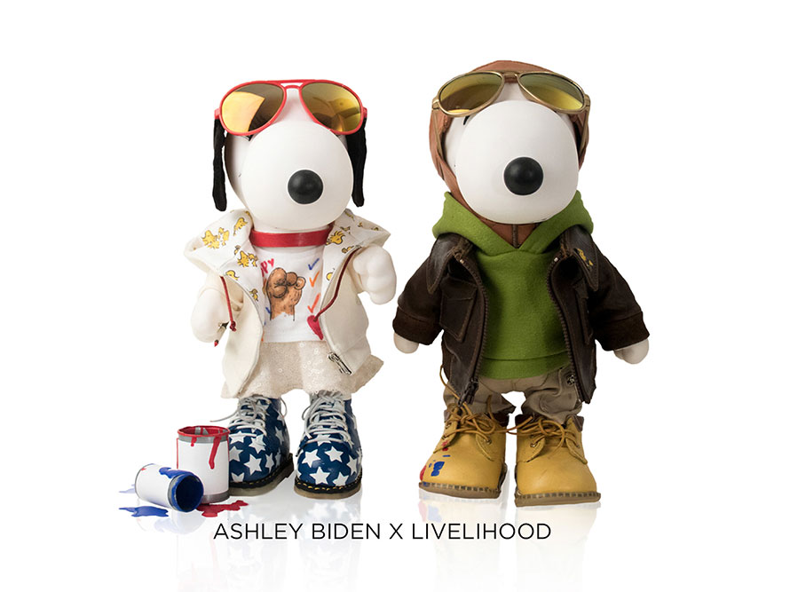 Two black and white, stuffed toy dogs standing in front of a white background. The dog on the left is wearing a beige outfit with red and gold aviators and the dog on the right is wearing a green hoodie, brown leather jacket and red and gold aviators.
