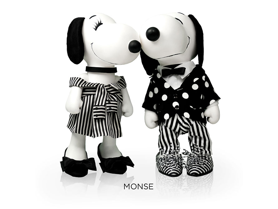 Two black and white, stuffed toy dogs in front of a white background. One is wearing a black and white striped dress and black high heels and the other one a black and white polka dot suit and a bow tie.