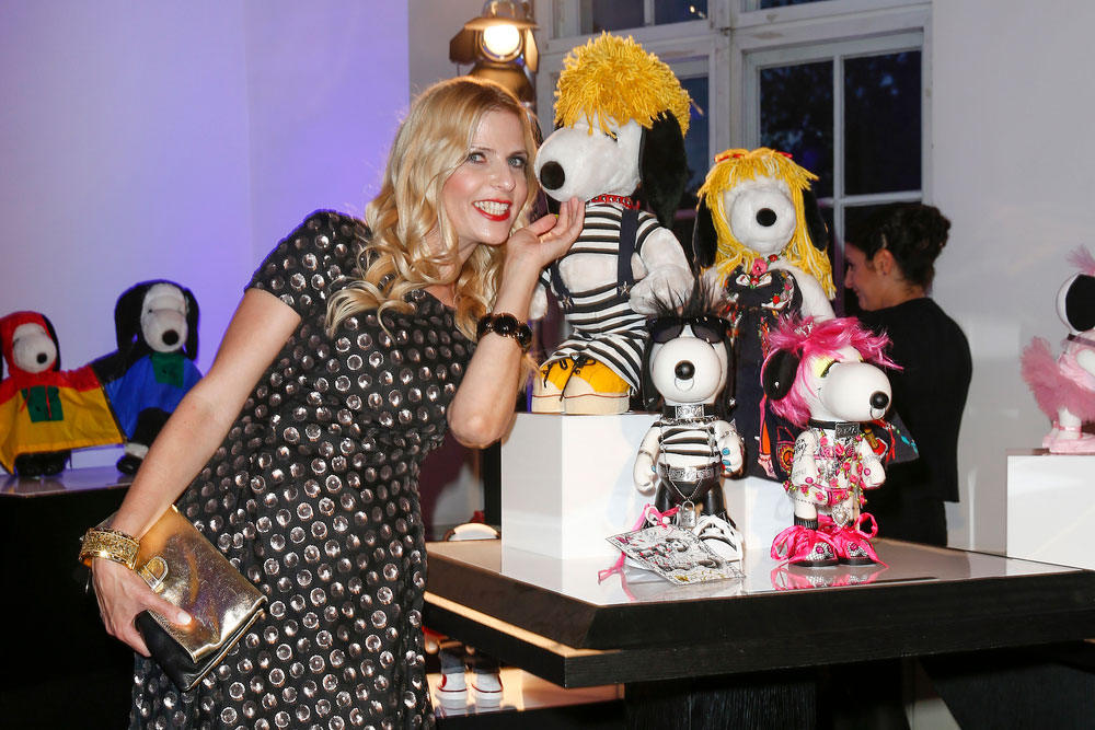 A blonde woman, wearing a black dress, leaning over towards a display of black and white dog statues at a semi formal event.
