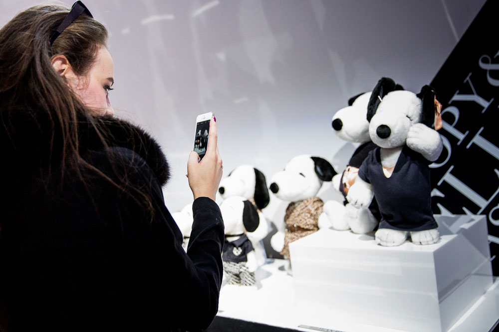 A brunette woman, wearing a black coat, taking a photo of black and white dog statues on display at a semi formal event.