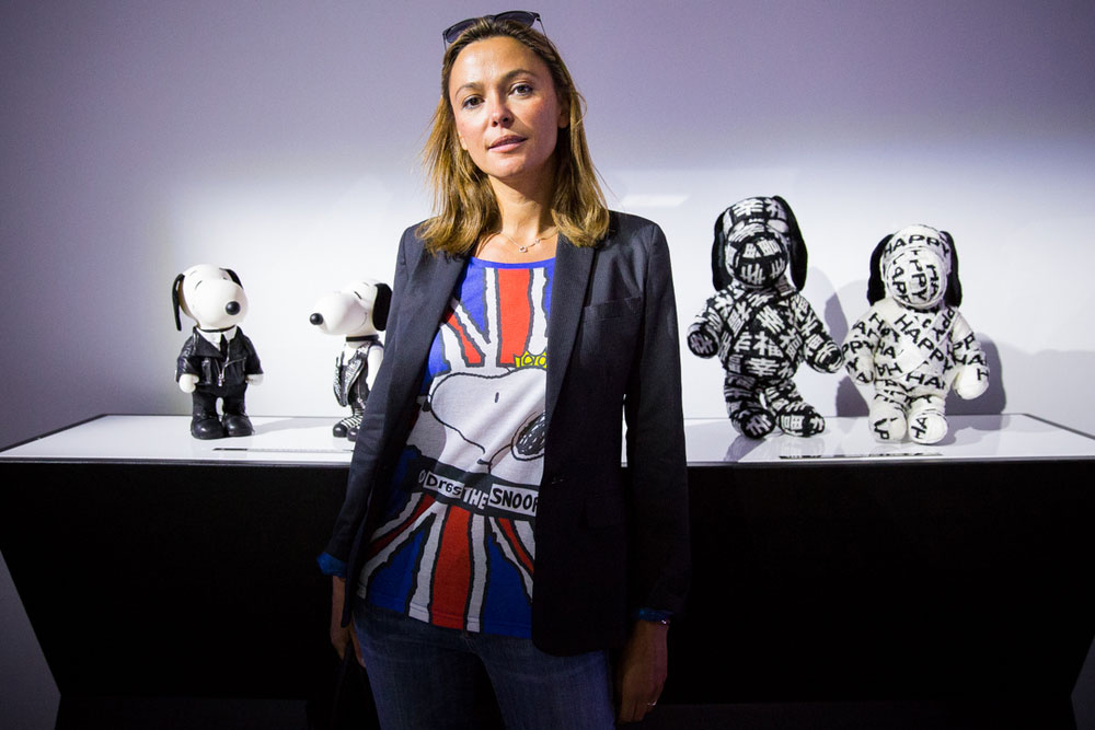 A woman with short light brown hair, wearing a black blazer and a colourful shirt, is posing for a photo in front of a display of black and white dog statues.