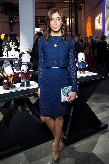 A brunette woman, wearing a navy blue dress, posing for a photo at a semi formal event. There is a display of black and white dog statues behind her.