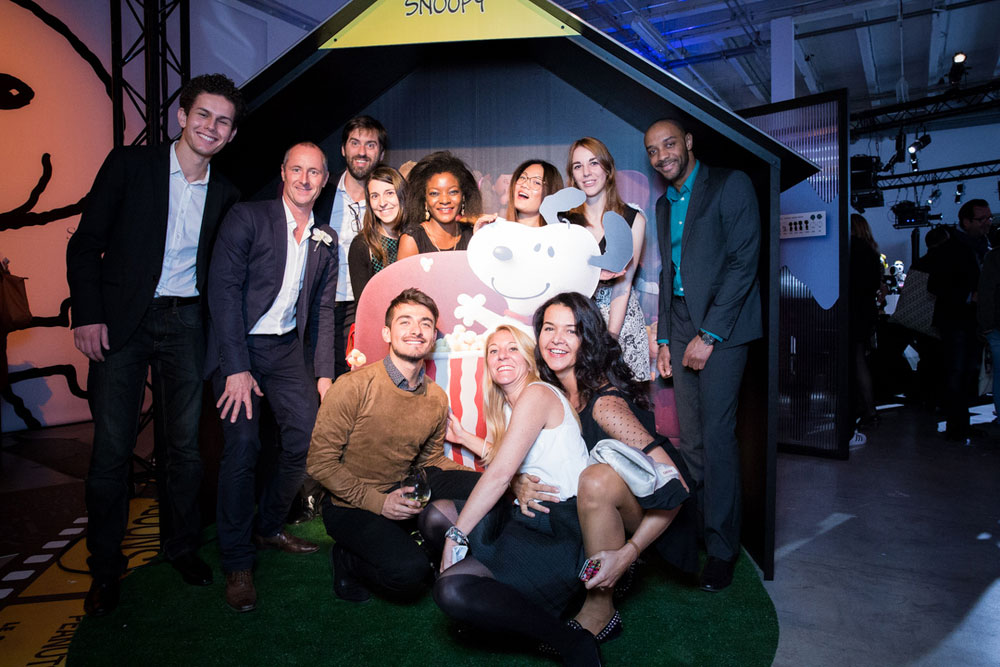 A large group of people dressed in semi formal attire posing for a photo at an indoor event, in front of a large playhouse.