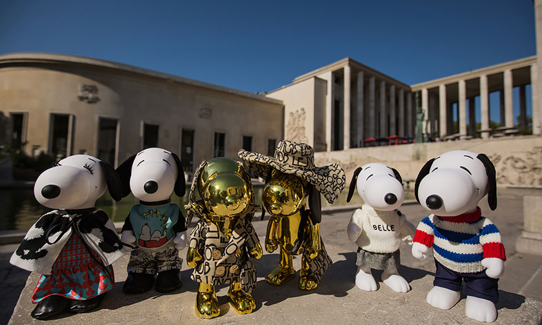 Four black and white dog statues and 2 gold dog statues on a concrete wall with a building in the background.