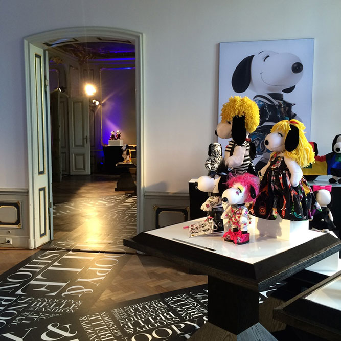 Small black and white dog statues, in various costumes, displayed in a large room. There is a photo on the wall of a black and white dog.