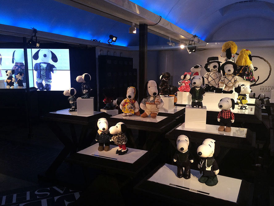 A dark, indoor space displaying small black and white dog statues wearing designer costumes.