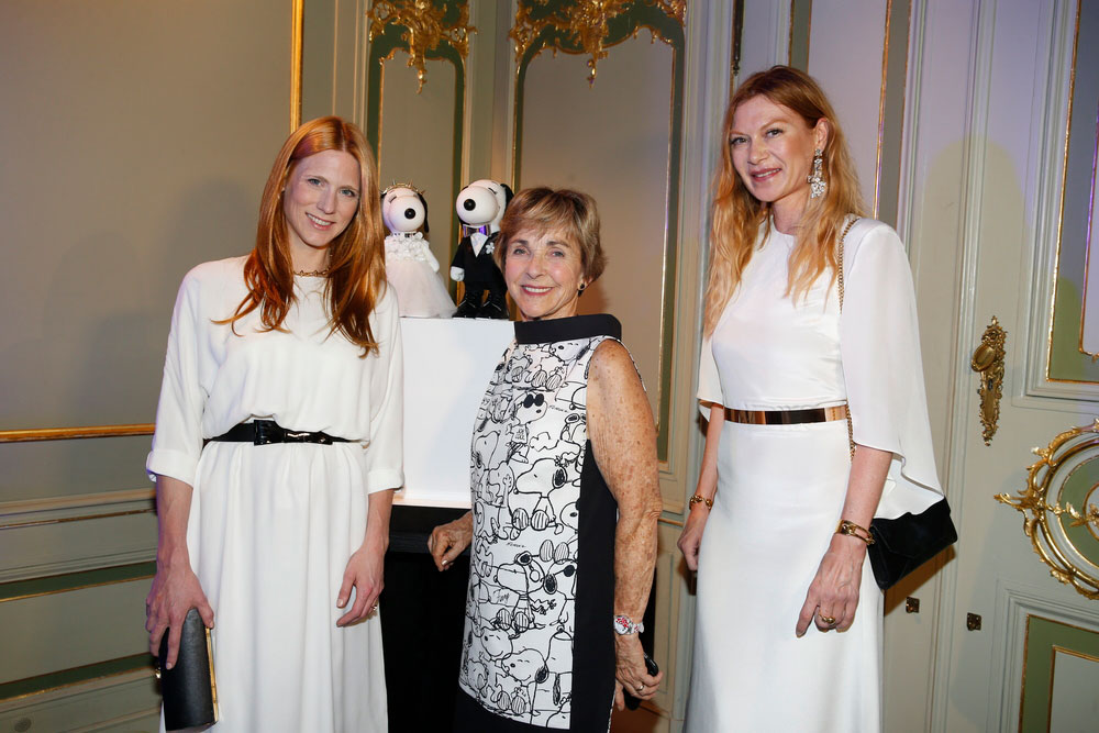 Three women, wearing white and black dresses, posing for a phot at an event.