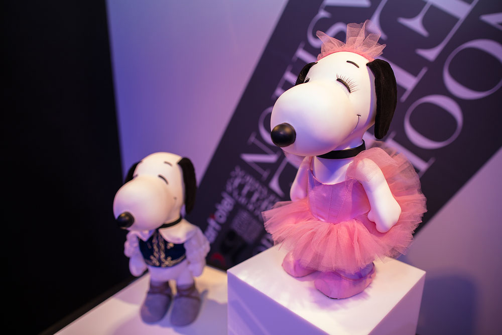 A close-up of two black and white dog statues on display in a room with blue lights. One statue is wearing a pink tulle dress and the other one a white blouse and a vest.