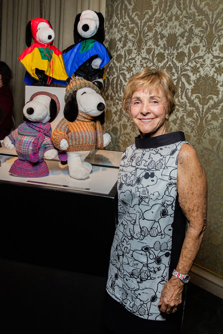 A senior woman, wearing a black and white dress, standing beside a display of black and white dog statues wearing various outfits.