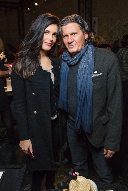 A brunette women in a black coat standing beside a man with long hair and a blue scarf and posing for a photo.