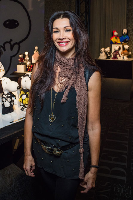 A tall, brunette woman wearing a black top and a brown scarf, smiling and posing for a photo at an event.