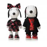 Two black and white dog statues in front of a white background. The dog on the left is wearing a checkered dress, shoes and a bow on her head. The dog on the right is wearing red shoes, red shirt and a black jacket.