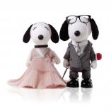 Two black and white dog statues  in front of a black and white background. The dog on the left is wearing a pink gown and the dog on the right is wearing a grey suit and glasses.