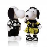 Two black and white dog statues in front of a white background. The dog on the left is wearing black pants and a black and white shirt. The dog on the right is wearing a black and yellow dress with black sandals.