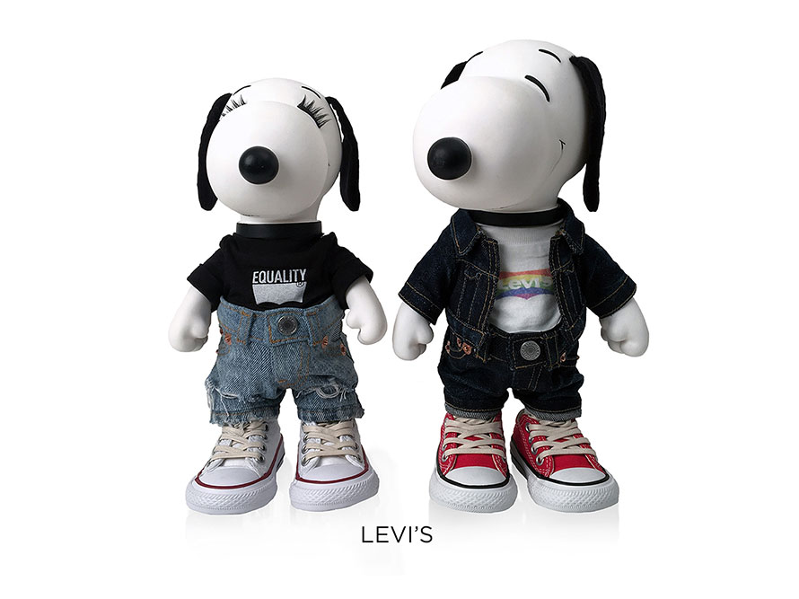 Two black and white, stuffed toy dogs standing in front of a white background. The dog on the left is wearing a black t-shirt and blue jeans and the dog on the right is wearing dark jeans and a jean jacket.