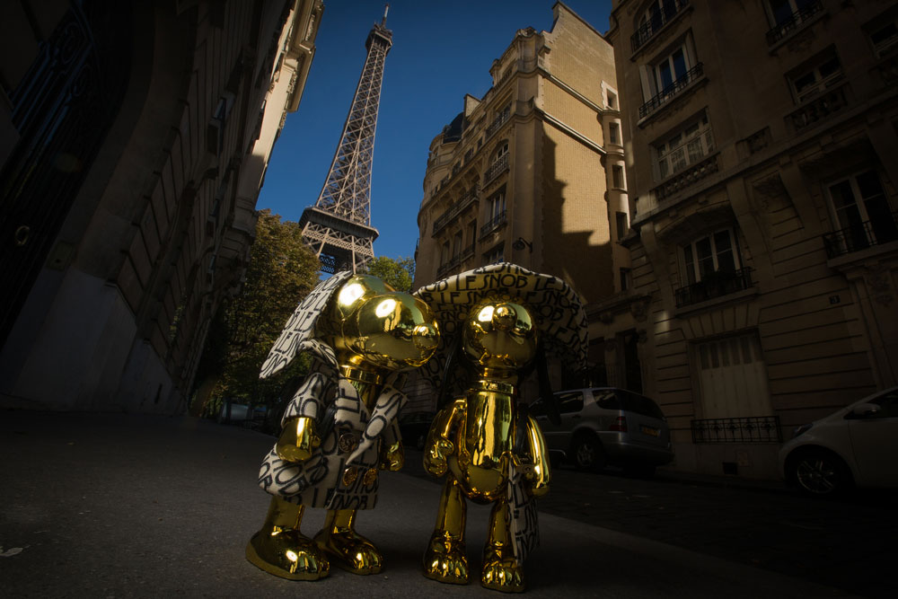 Two gold, dog statues in the middle of a residential street in Paris with the Eiffel tower in the background.