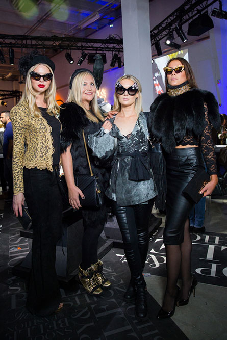 Four women, in semi formal attire, posing for a photo at an event. Three of the women are wearing unique sunglasses.
