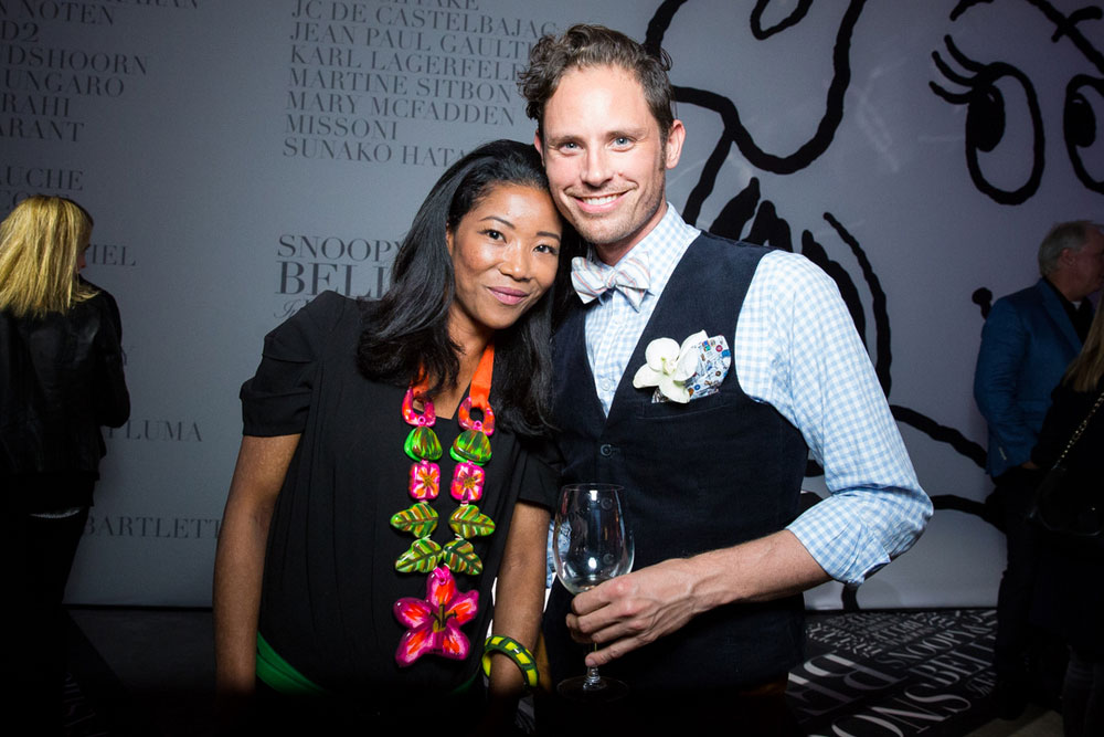A man and  woman, dressed in semi formal attire, posing for a photo at an event. The man is holding a wine glass in his hand.
