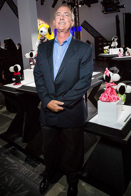 A middle aged man with grey hair, wearing a blue suit, posing for a photo at an indoor event. He is standing in front of a display of black and white dog statues.
