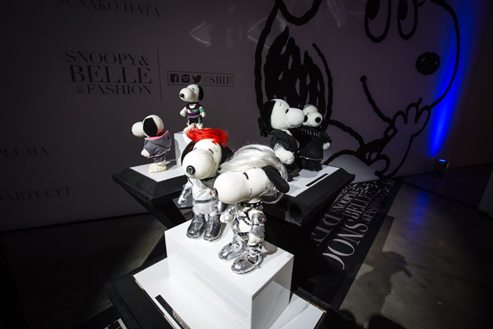 Black and white dog statues, wearing various costumes, on display in a darkly lit room.