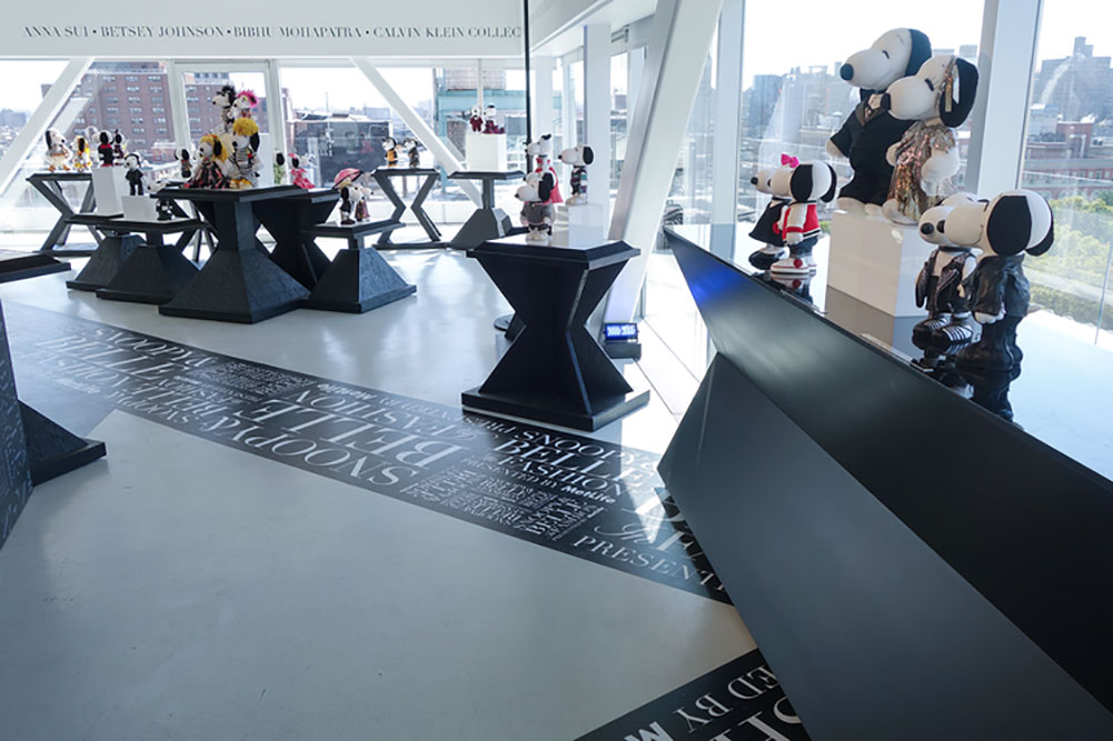 A bright indoor space with large windows and a bunch of tables displaying small, black and white dog statues wearing designer costumes.