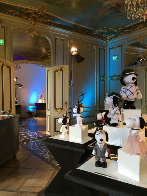 Small black and white dog statues displayed on white tables inside a room with antique furniture and a crystal chandelier.