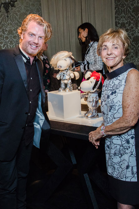 A man and senior woman, dressed in semi-formal attire, standing in front of dog statues and posing for a photo at an event.