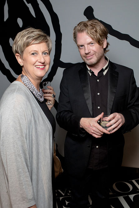 A middle-aged woman with short blonde hair is standing next to a blonde man wearing a black suit. They are posing for a photo at an event.
