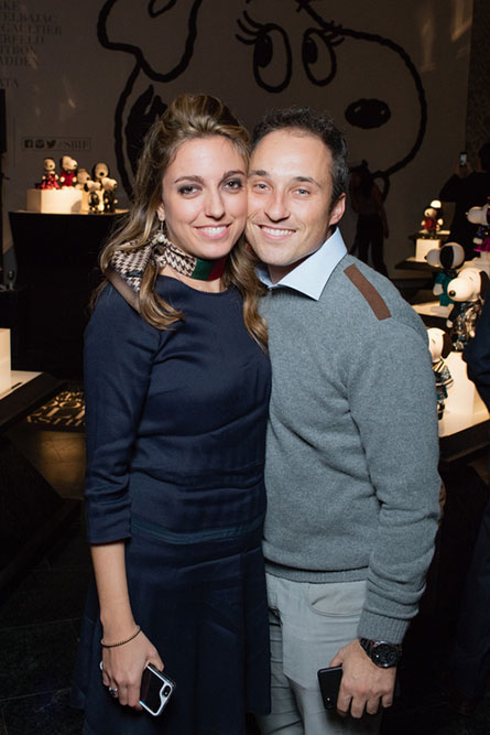 A woman wearing a navy blue dress is standing next to a man wearing a grey sweater. They are posing for a photo at a semi formal event.