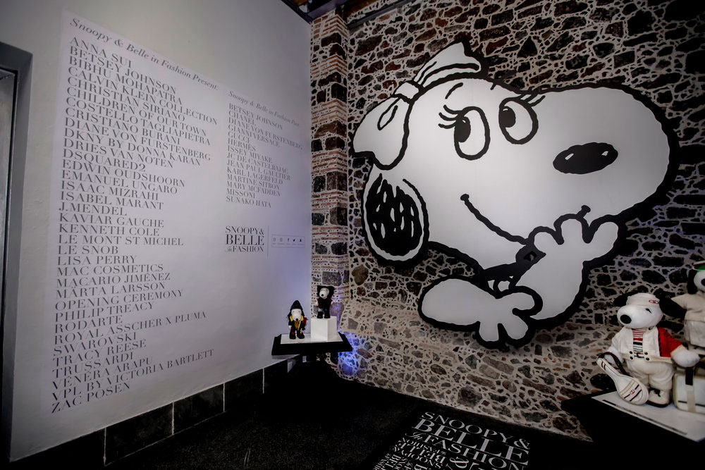 A indoor space with a long list of names written on a white wall and an art piece of a black and white dog hanging on the wall.