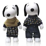 Two black and white dog statues in front of a white wall. The dog on the left is wearing a beige sweater  and a checkered skirt and the dog on the right is wearing jeans and a checkered sweater.