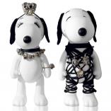 Two black and white dog statues in front of a white background. The dog on the left is wearing a crown, a necklace and a bracelet. The dog on the right is wearing a black outfit made of strings.