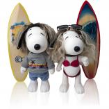 Two black and white dog statues in front of two surfboards and a white background. The dog on the left is wearing a grey shirt and jean shorts and the dog on the right is wearing a red bikini.