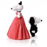 Two black and white dog statues in front of a white background. The dog on the left is a bit taller and wearing a long pink dress. The dog on the right is wearing a black and white tuxedo.