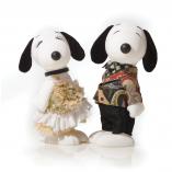 Two black and white dog statues in front of a white background. The dog on the left is wearing a fluffy, white and beige dress. The dog on the right is wearing black pants and a colourful jacket.