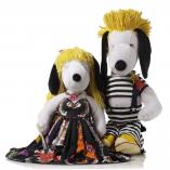 Two black and white dog statues standing beside each other in front of a white background. The dog on the left is wearing a yellow wig and a long black and orange dress. The dog on the right is wearing a yellow wig and a black and white, striped outfit.