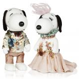 Two black and white dog statues in front of a white background. The dog on the left is wearing a floral suit jacket and beige pants and the dog on the right is wearing a sparkly, beige gown.